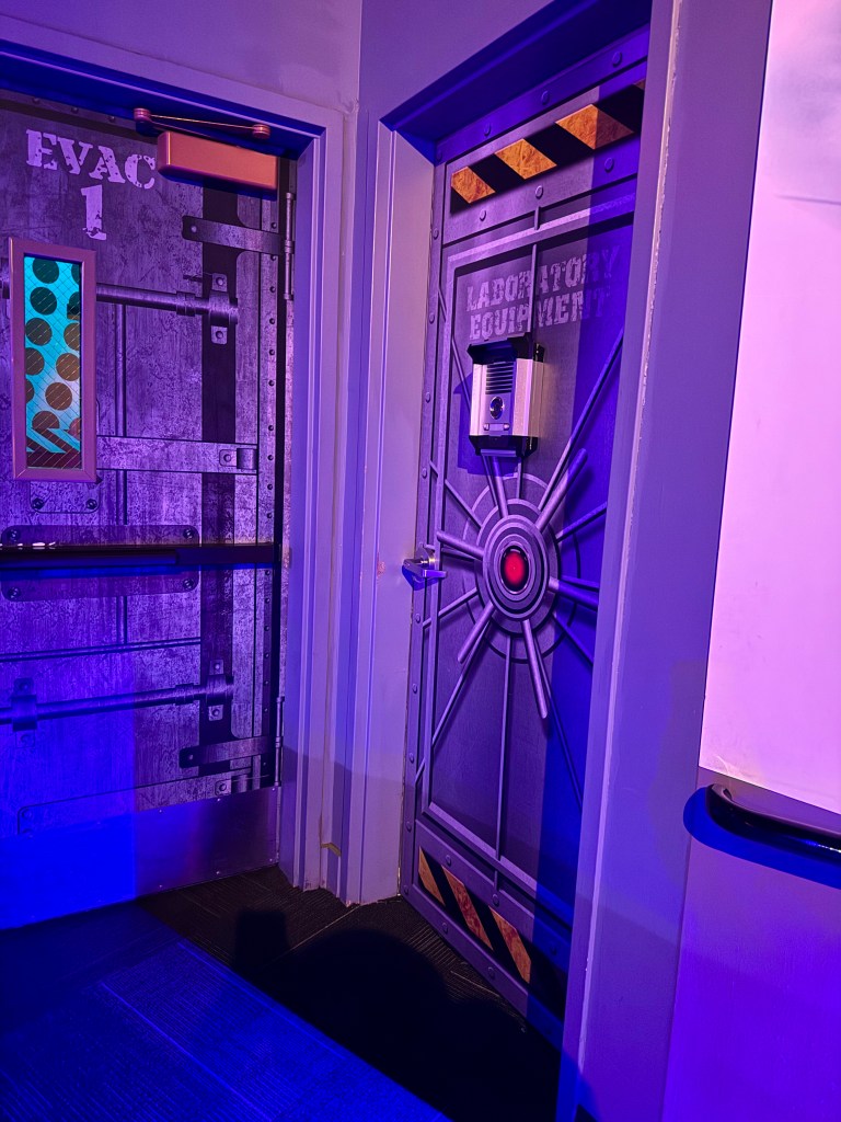 Interior view of two doors labeled 'EVAC 1' and 'LABORATORY EQUIPMENT,' featuring industrial design elements and purple lighting.