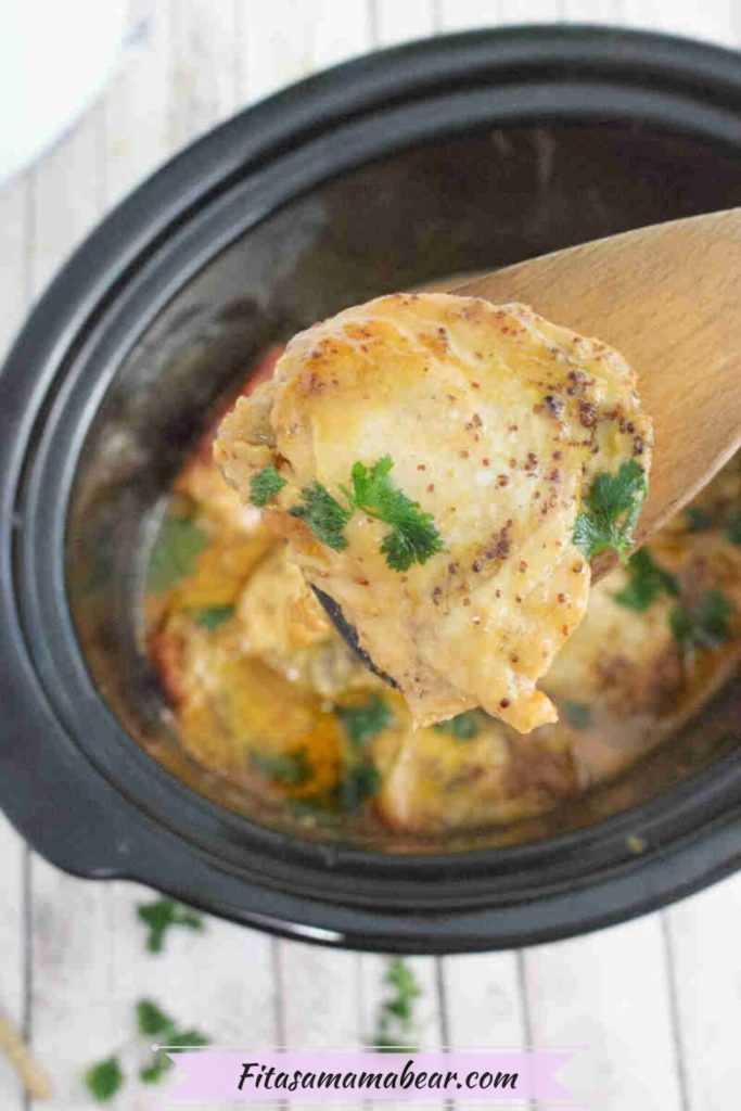 A close-up of a wooden spoon lifting a piece of creamy chicken from a slow cooker, garnished with fresh parsley.