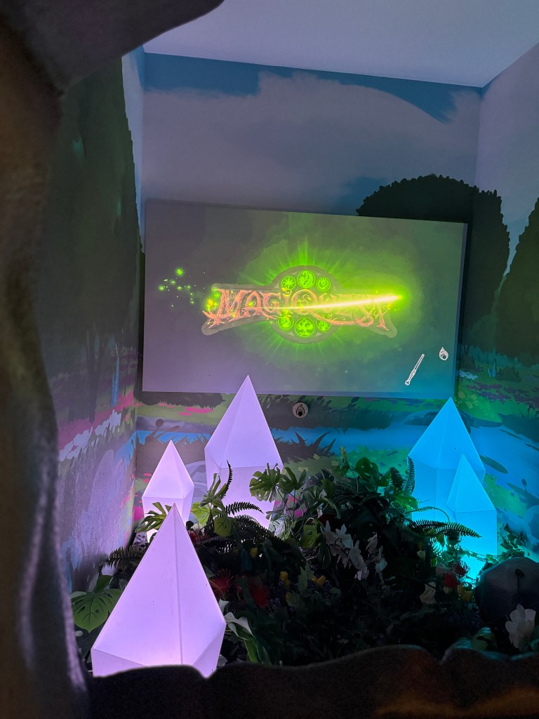 A colorful, illuminated display featuring the word 'MagiQuest' surrounded by glowing crystals and lush foliage in a themed room. Great Wolf Lodge in Grapevine, TX. 