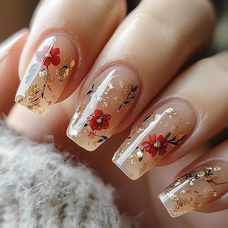 Nails featuring a natural nude base with red floral designs and gold glitter accents, providing a warm and autumnal vibe.