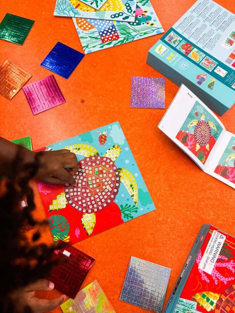Child completing a numbered turtle mosaic with sticker sheets and instructions nearby.