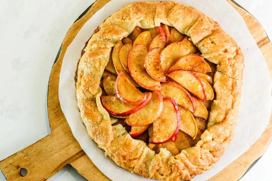 A freshly baked apple galette featuring golden and red apple slices arranged beautifully on a flaky, rustic crust, presented on a wooden serving board.