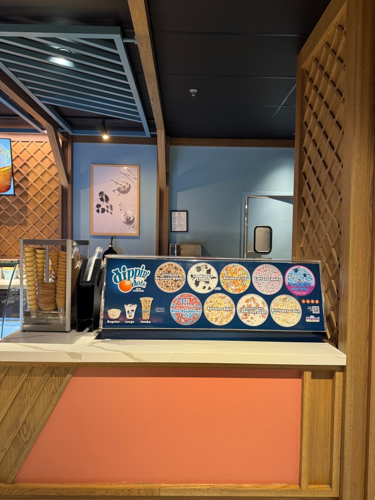 Interior view of a Dippin' Dots ice cream shop featuring a menu board with various flavors and options, a brightly colored counter, and wooden accents in the decor.