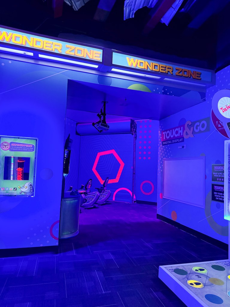 Interior view of the 'Wonder Zone' with vibrant blue lighting, featuring interactive digital displays and seating area.