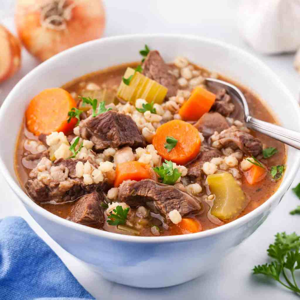 A hearty bowl of beef and barley soup featuring tender chunks of beef, carrots, celery, and barley in a rich broth, garnished with fresh parsley.