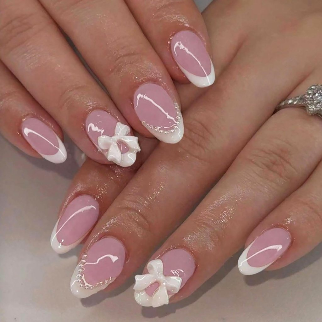 Close-up of manicured nails featuring a pink base with white tips, adorned with decorative white bows and delicate beading.