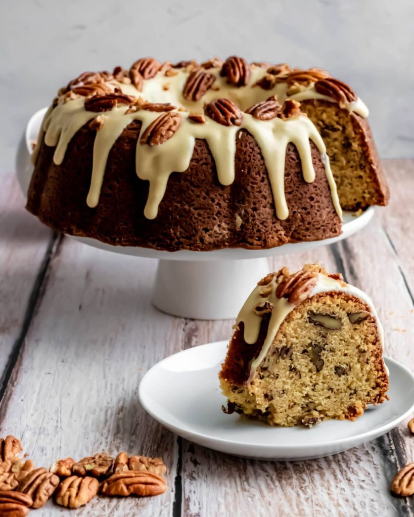 A moist Maple Pecan Bundt Cake topped with a creamy glaze and garnished with pecans, served on a white plate.