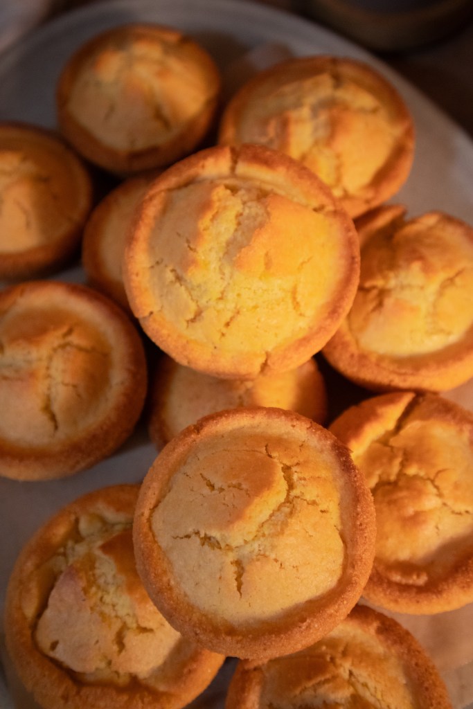 A close-up of freshly baked golden cornbread muffins stacked on a plate.
