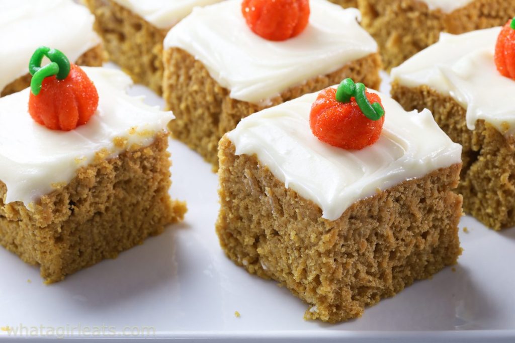 Close-up of pumpkin spice cake squares topped with cream cheese frosting and decorated with miniature pumpkin candy.