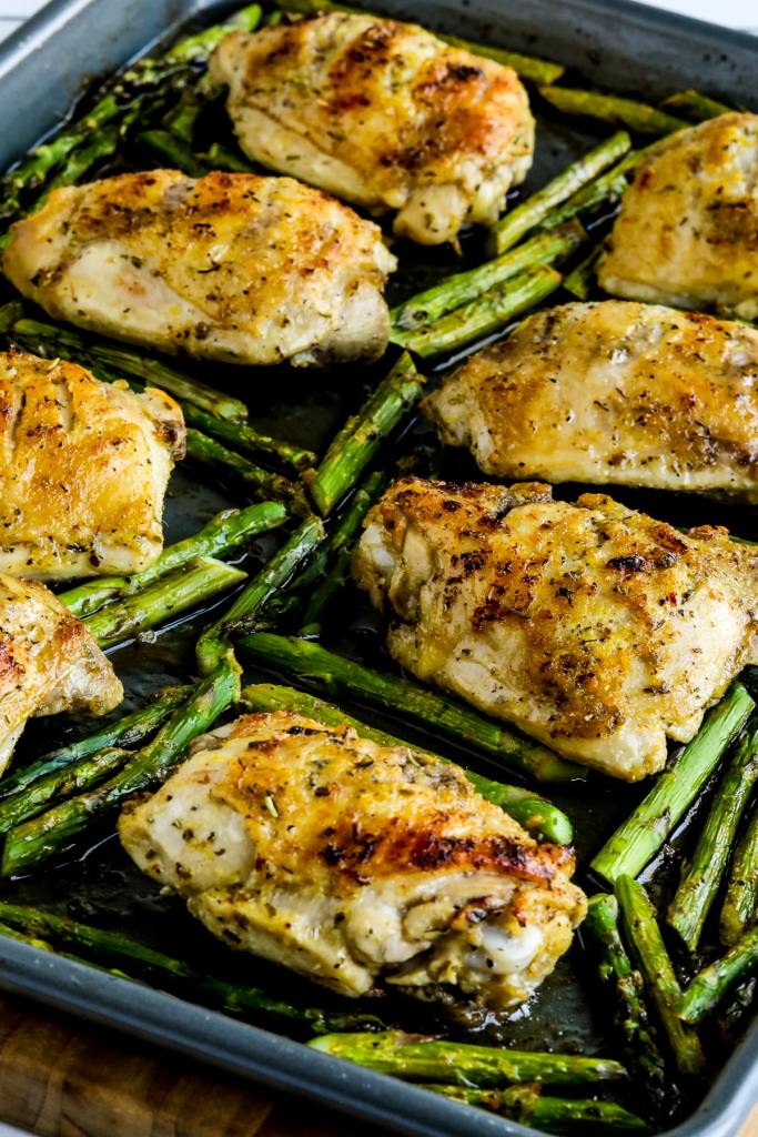 Baked chicken thighs seasoned with herbs, placed on a sheet pan alongside roasted asparagus.