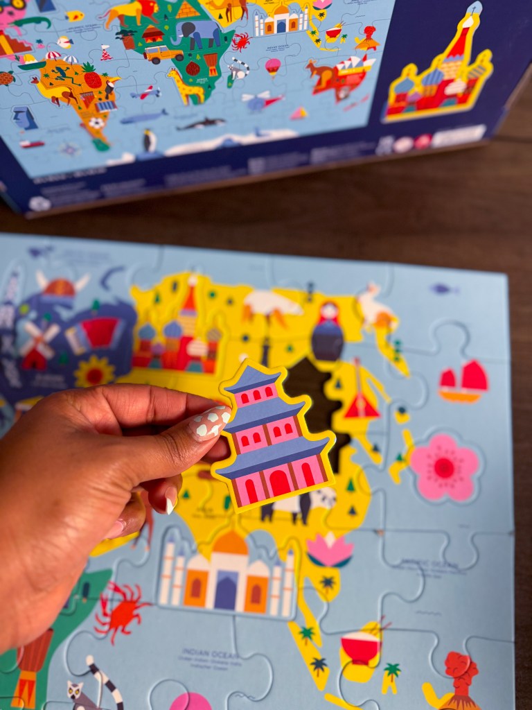 Hand holding an Asian landmark puzzle piece above the Asia section of a world map puzzle.