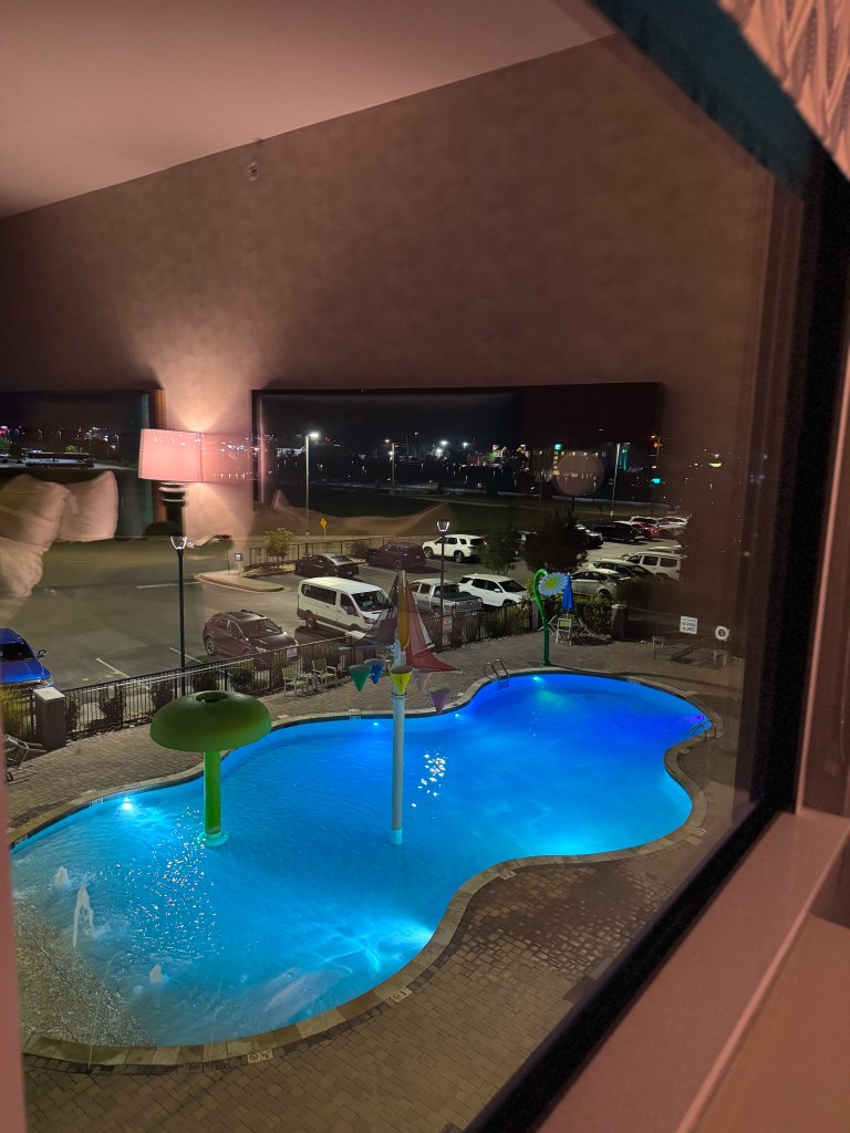 Outdoor swimming pool with colorful water features illuminated at night at Home2 Suites Pigeon Forge.