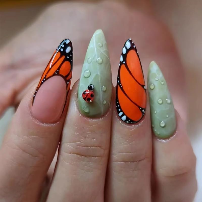 Close-up of hands displaying creatively designed nails featuring orange butterfly patterns and a ladybug accent on a green nail.