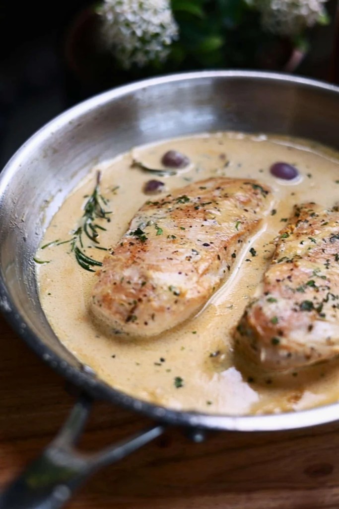 Cooked chicken breasts in a creamy sauce with herbs, placed in a skillet.