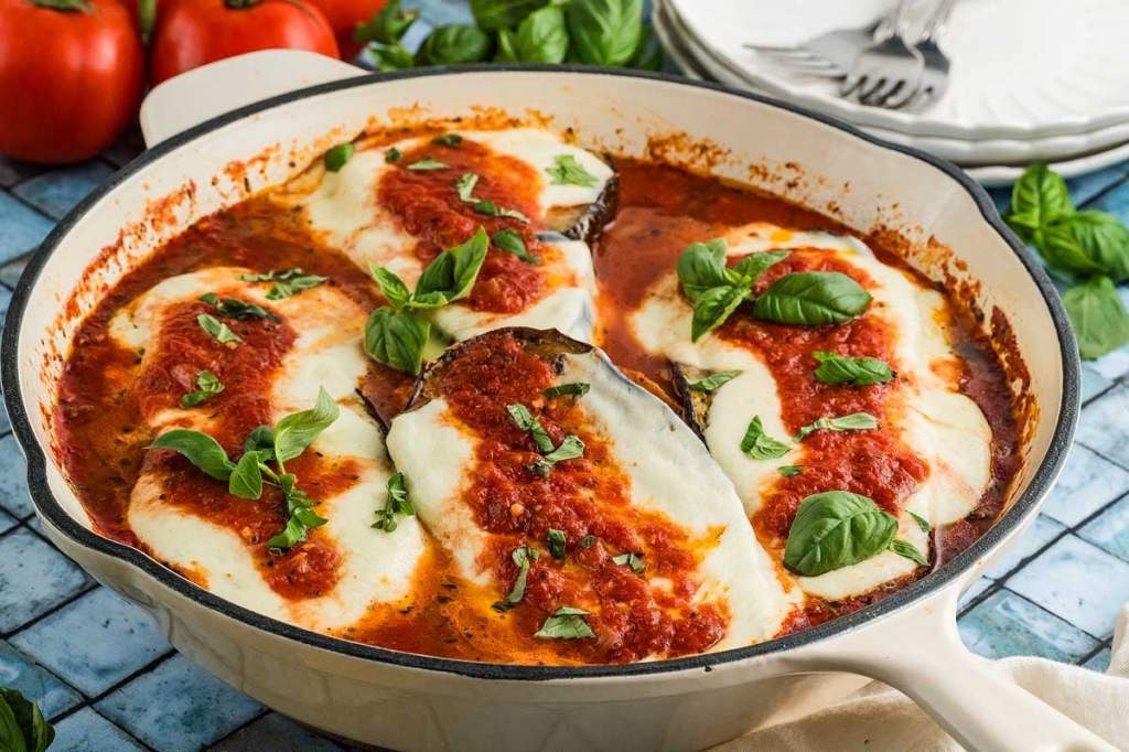 A dish of baked chicken topped with marinara sauce, melted mozzarella cheese, and fresh basil leaves, served in a cream-colored casserole dish.