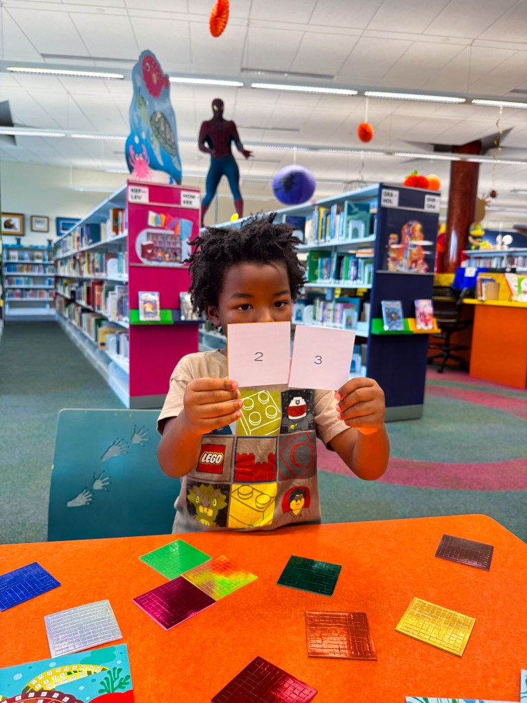 Kindergartner holding numbered cards while completing a hands-on number recognition activity.