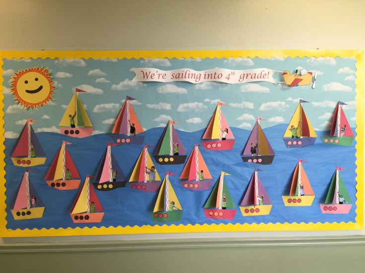 A colorful classroom bulletin board featuring paper boats of various colors sailing on a blue background with clouds. The text reads 'We're sailing into 4th grade!' along with a smiling sun.