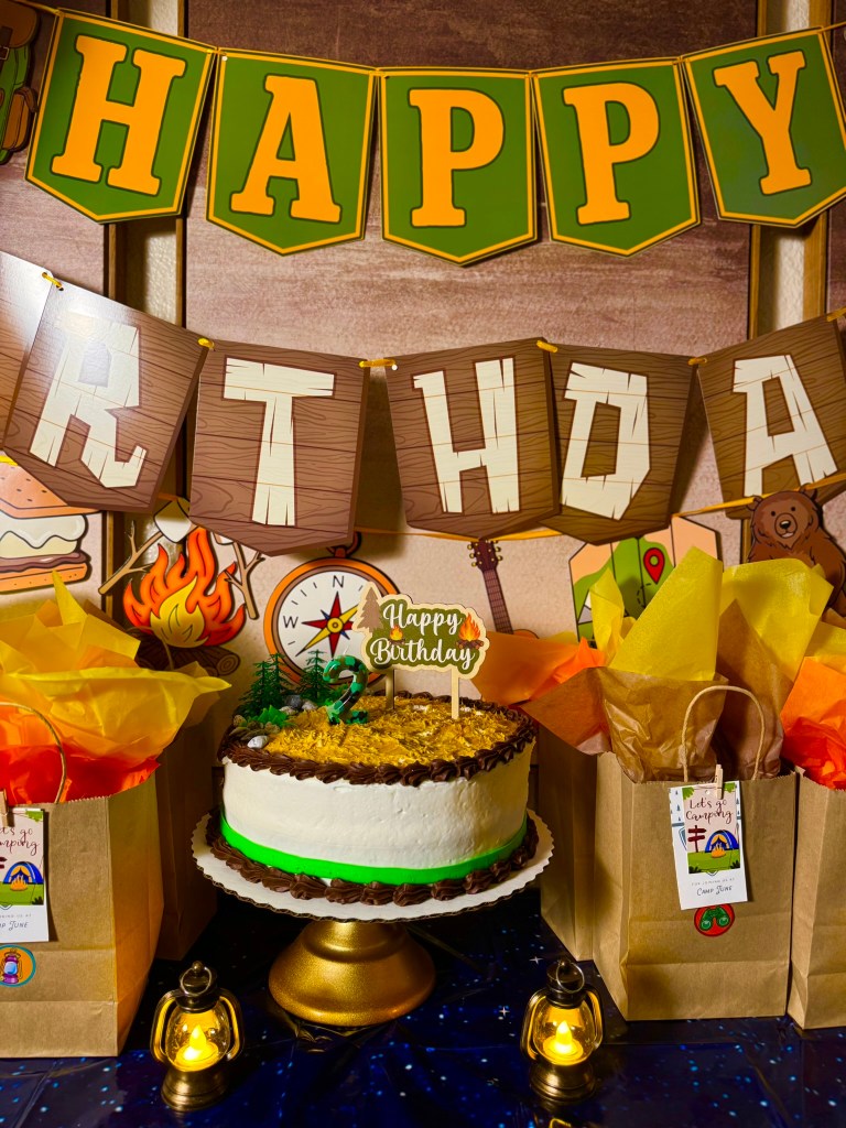 Toddler camping birthday cake with green number two candle, mini trees, rocks, and camping cake topper.