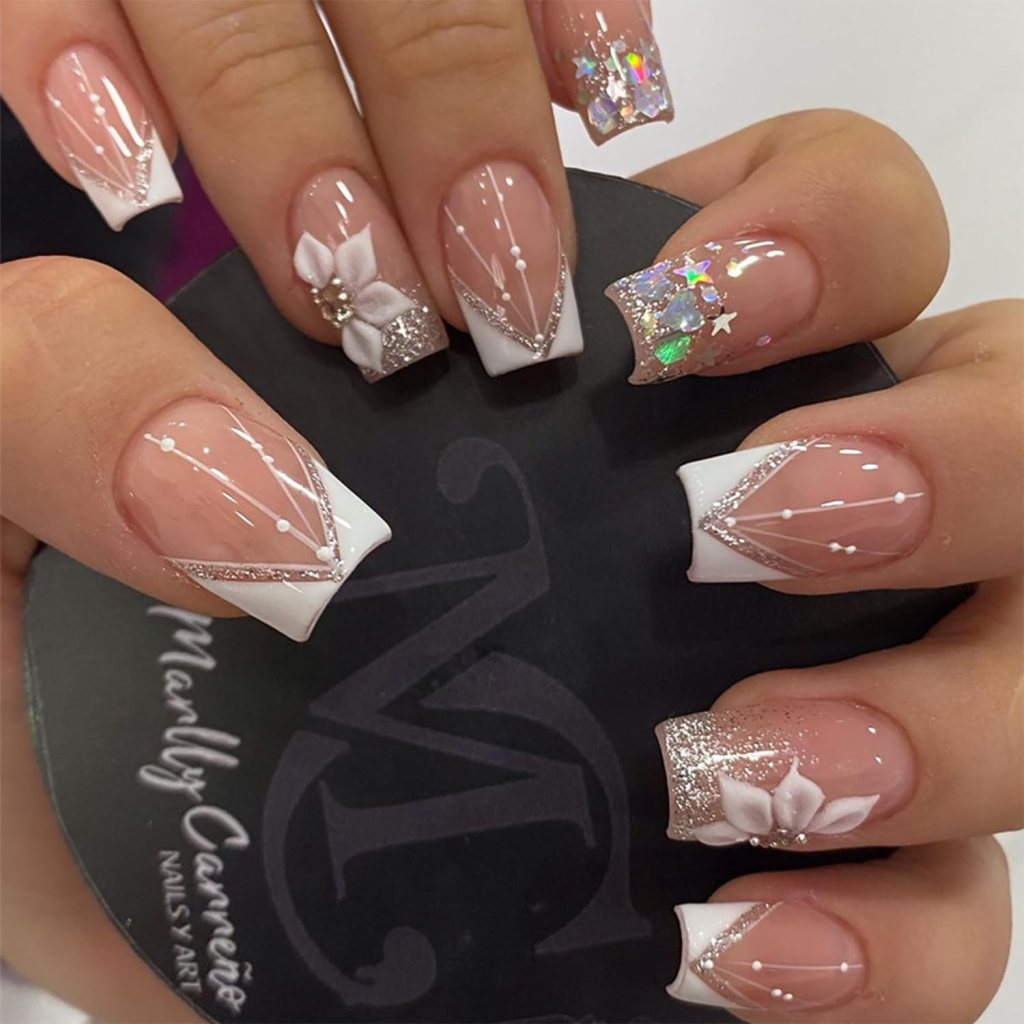 Close-up of elegantly manicured nails featuring a nude base, white tips, silver accents, and floral designs. One nail sparkles with holographic glitters.