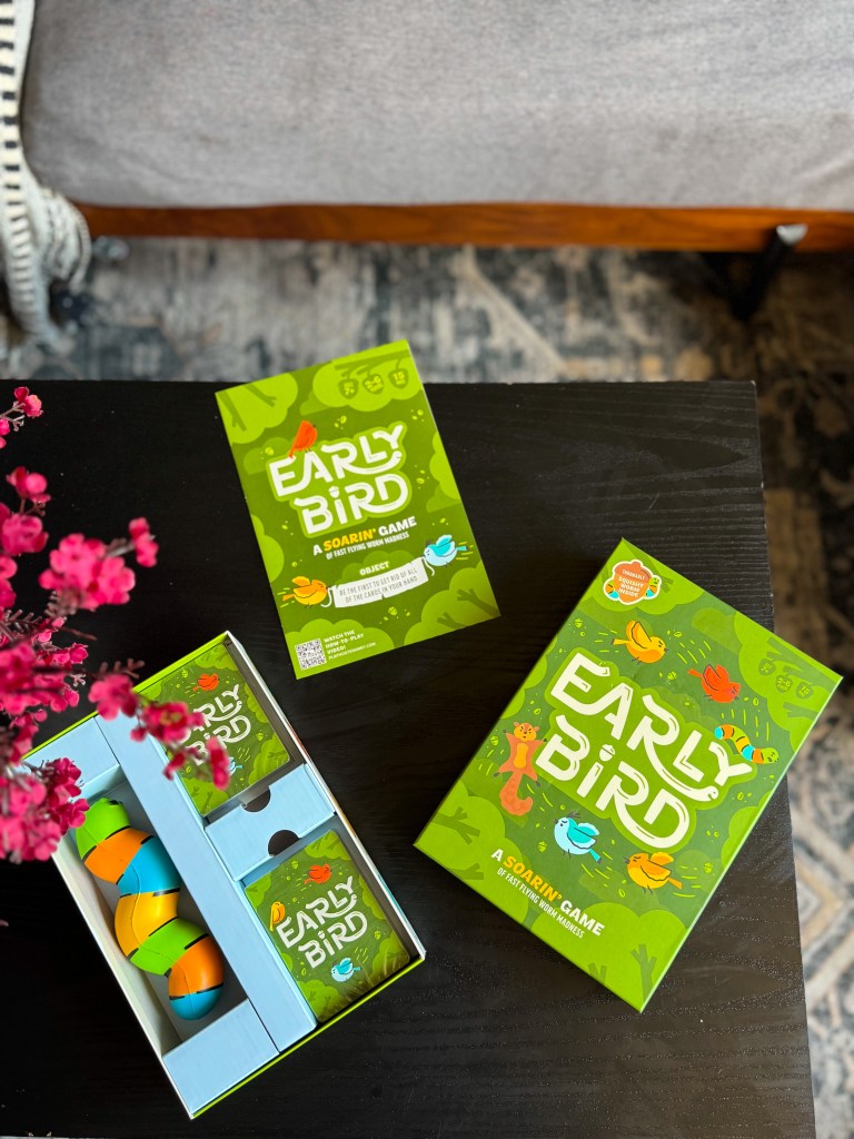 Early Bird strategy card game box displayed on a black table with pink flowers