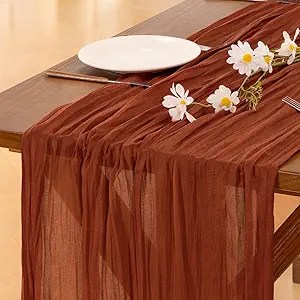 A beautifully styled table featuring a rust-colored table runner and a white plate, adorned with small white flowers, creating an inviting Thanksgiving decor.