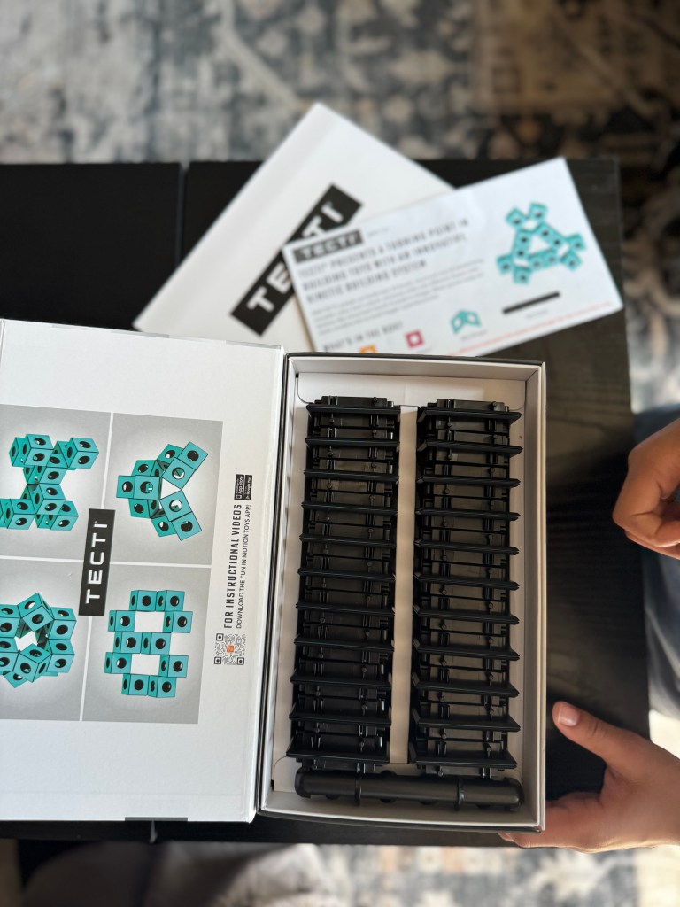 Interior view of a Tecti building kit box showing turquoise cubes and black connectors, along with an instruction booklet.