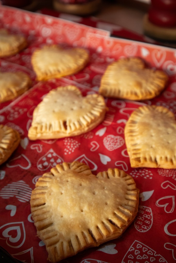 Baked heart-shaped pastries arranged on red parchment paper with a heart pattern.
