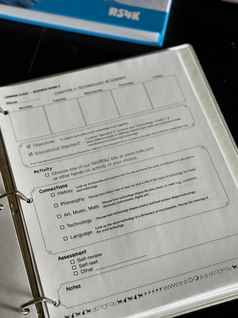 A close-up of a lesson plan page for 'Technology in Science' from Real Science 4 Kids Book 6, showing sections for objectives, activities, connections to other subjects, assessments, and notes, placed on a dark surface with part of the textbook visible in the background.