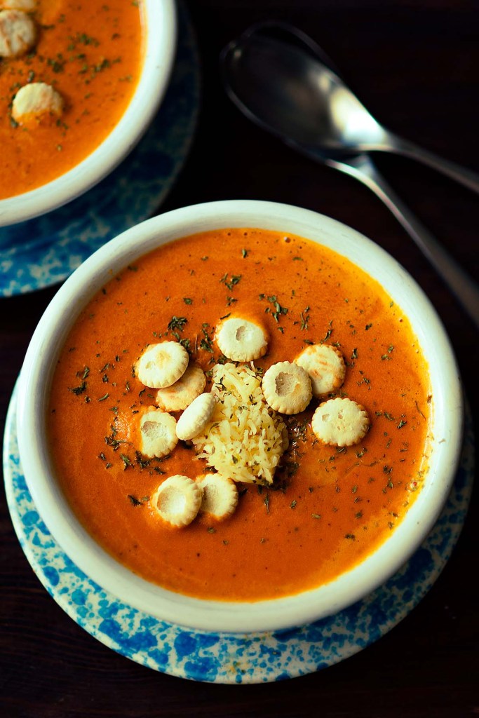 Creamy roasted red pepper gouda soup topped with shredded cheese and oyster crackers served in a rustic bowl