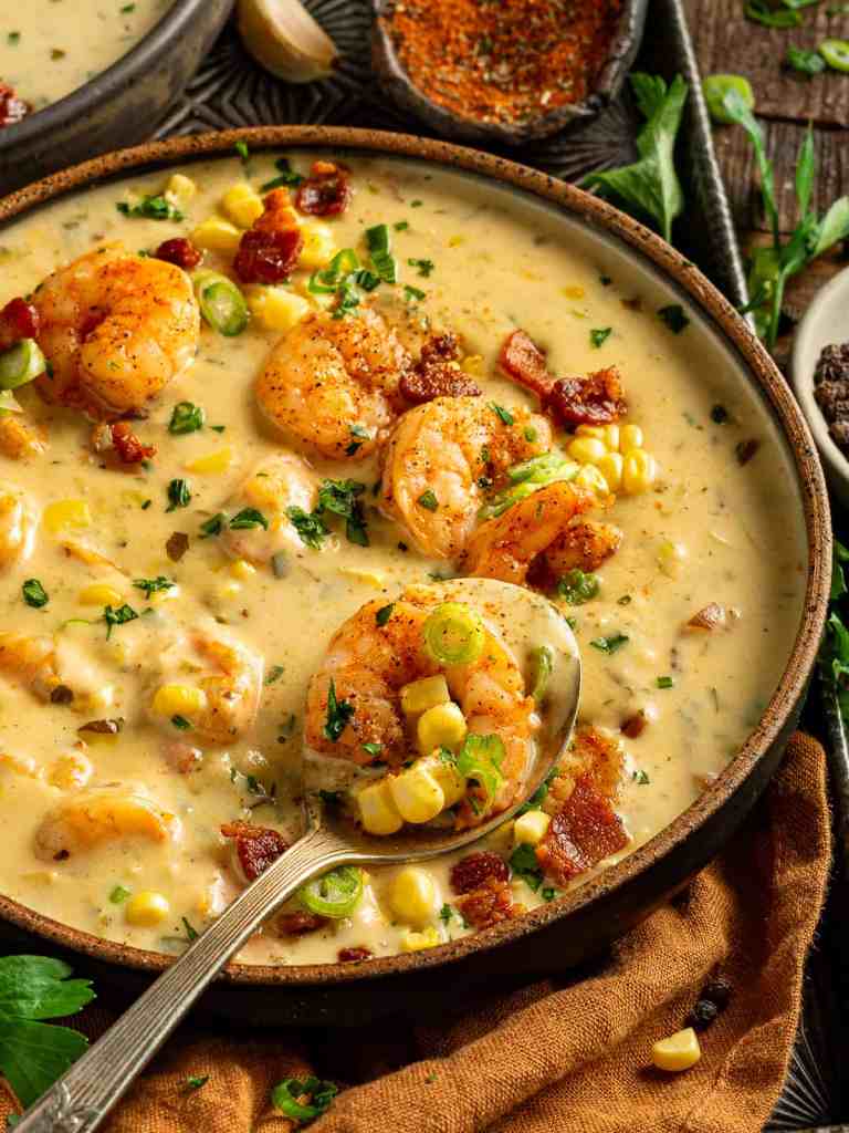 A bowl of creamy shrimp and corn bisque garnished with crispy bacon bits and green onions, served with a spoon.
