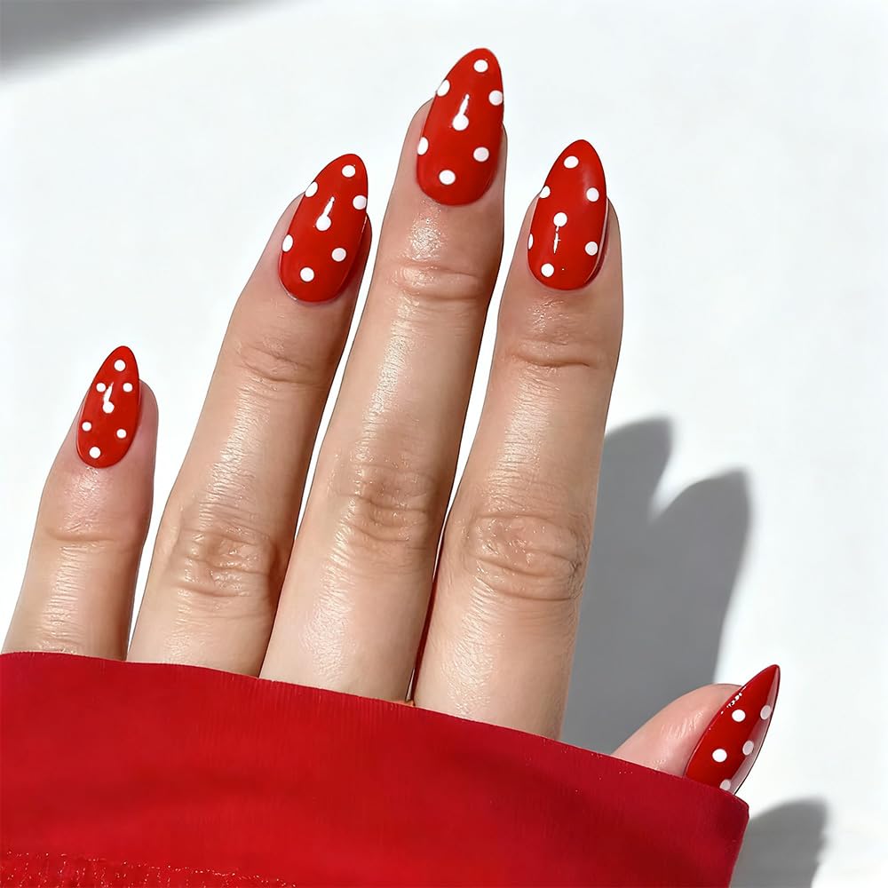 Close-up of a hand with red almond-shaped nails adorned with white polka dots, resting on a surface.