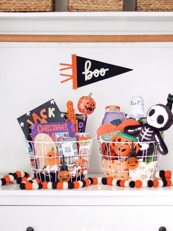 Two festive boo baskets filled with Halloween goodies, including books, toys, and decorations, are displayed alongside a playful 'boo' pennant banner.