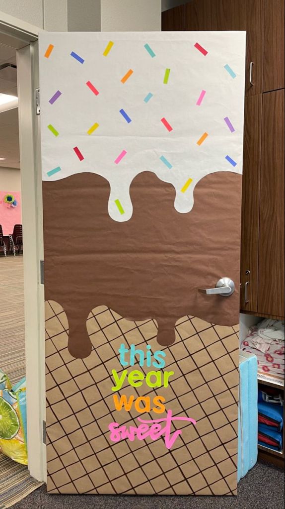 A decorated door featuring an ice cream theme with white icing, colorful sprinkles, and a brown cone design, along with the text 'this year was sweet' in vibrant colors.