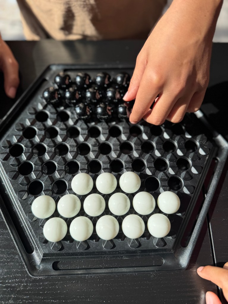 Close-up of hands moving black and white marbles on a hexagonal board of the game Abalone.