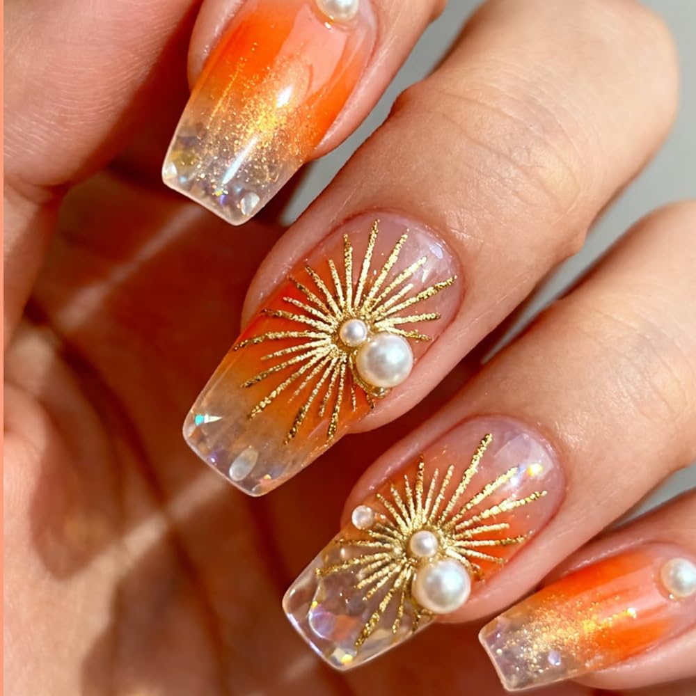 Orange ombre acrylic nails with gold sunburst nail art and pearl embellishments