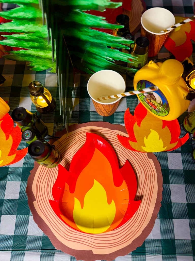 Camping birthday party place setting with a fire plate on a log placemat and campfire napkin.