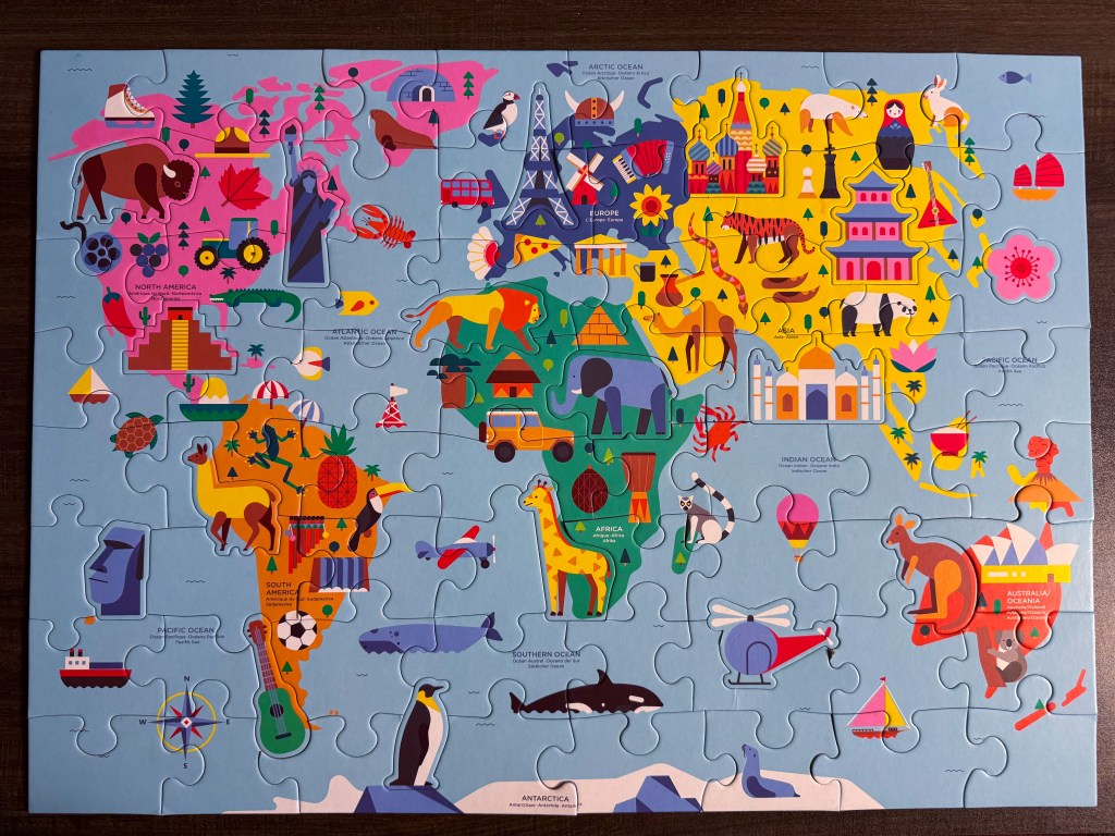 Completed world geography puzzle showing Africa, Asia, Australia and illustrated landmarks and animals.