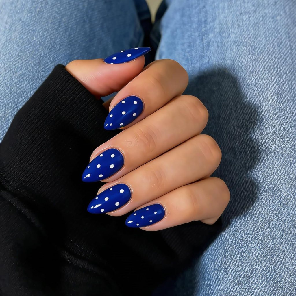 Blue polka dot almond nails with glossy cobalt blue polish and white dotted nail art design.