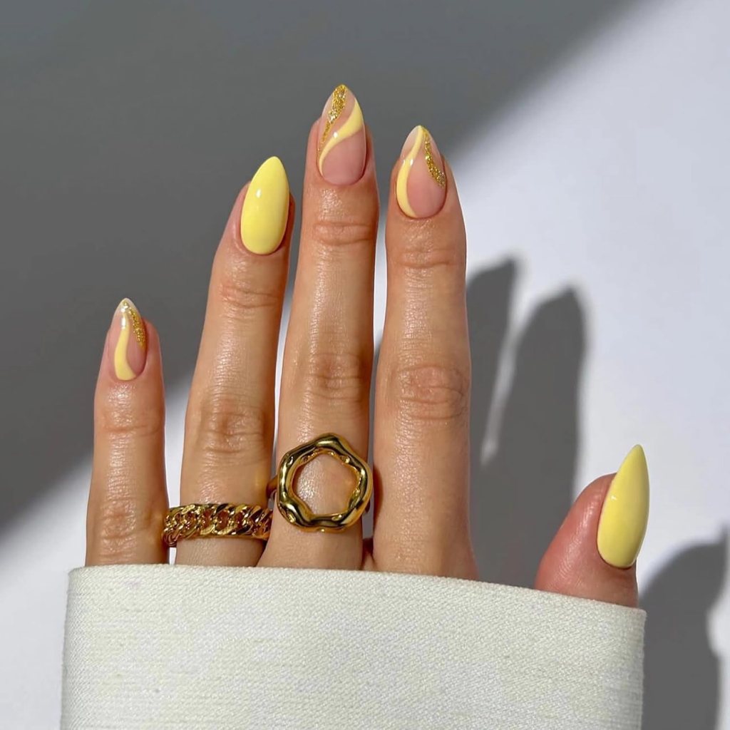 Butter yellow swirl nails with gold glitter accents and glossy abstract almond manicure design