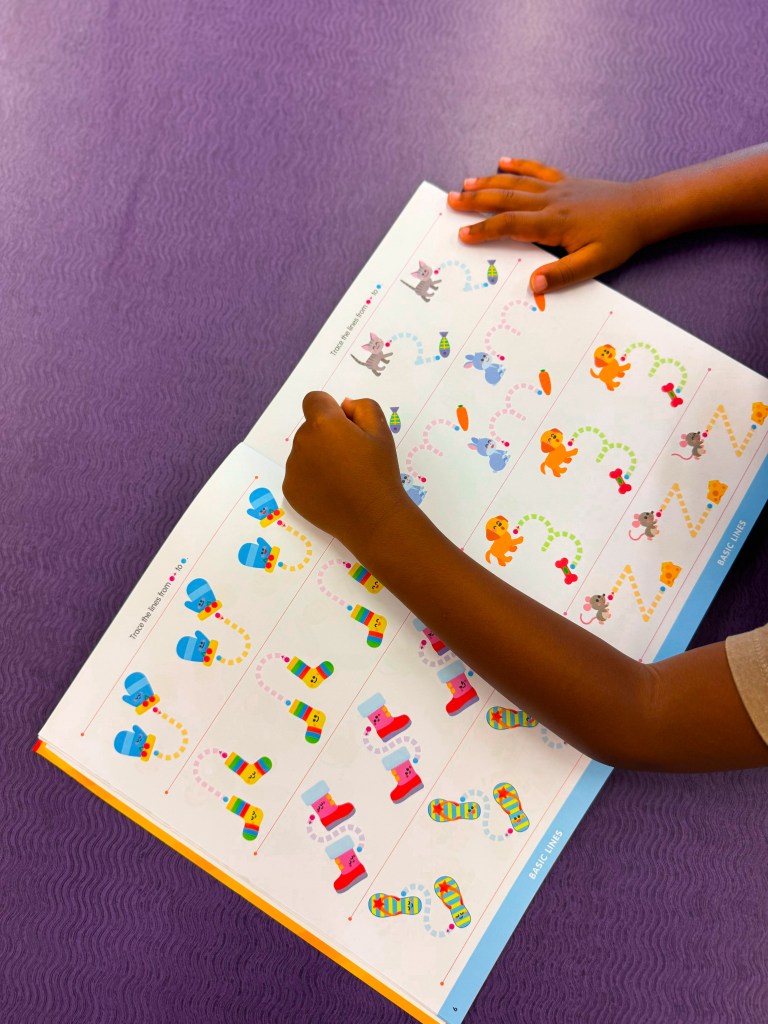 A child's hand drawing on a colorful activity book featuring various cartoon animals and objects, with a playful layout and engaging designs.