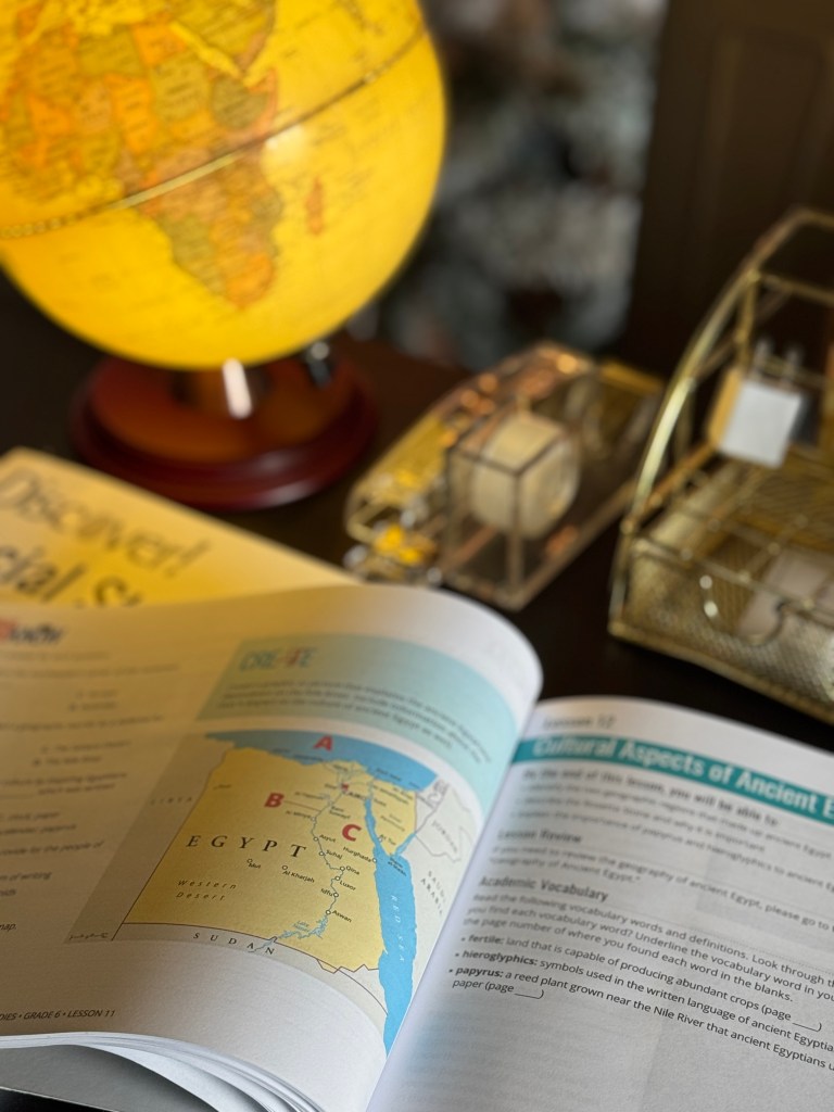 A glowing globe on a table next to an open textbook featuring a map of Egypt and lessons about Ancient Egypt.