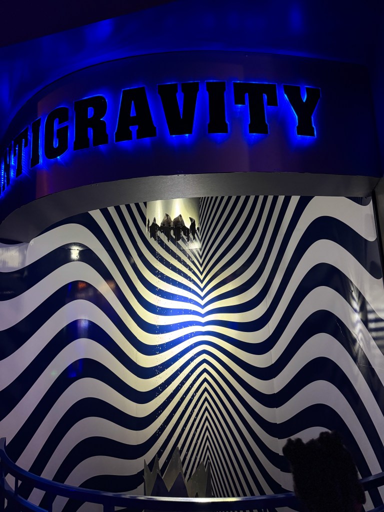 Colorful installation featuring the word 'ANTIGRAVITY' illuminated in blue, with a swirling blue and white striped pattern in the background.