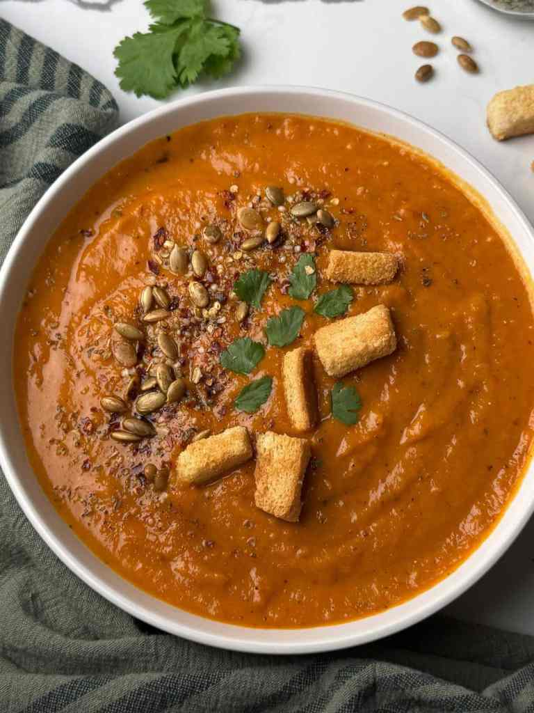 Velvety roasted red pepper and sweet potato soup topped with crunchy croutons and sunflower seeds served in a rustic bowl