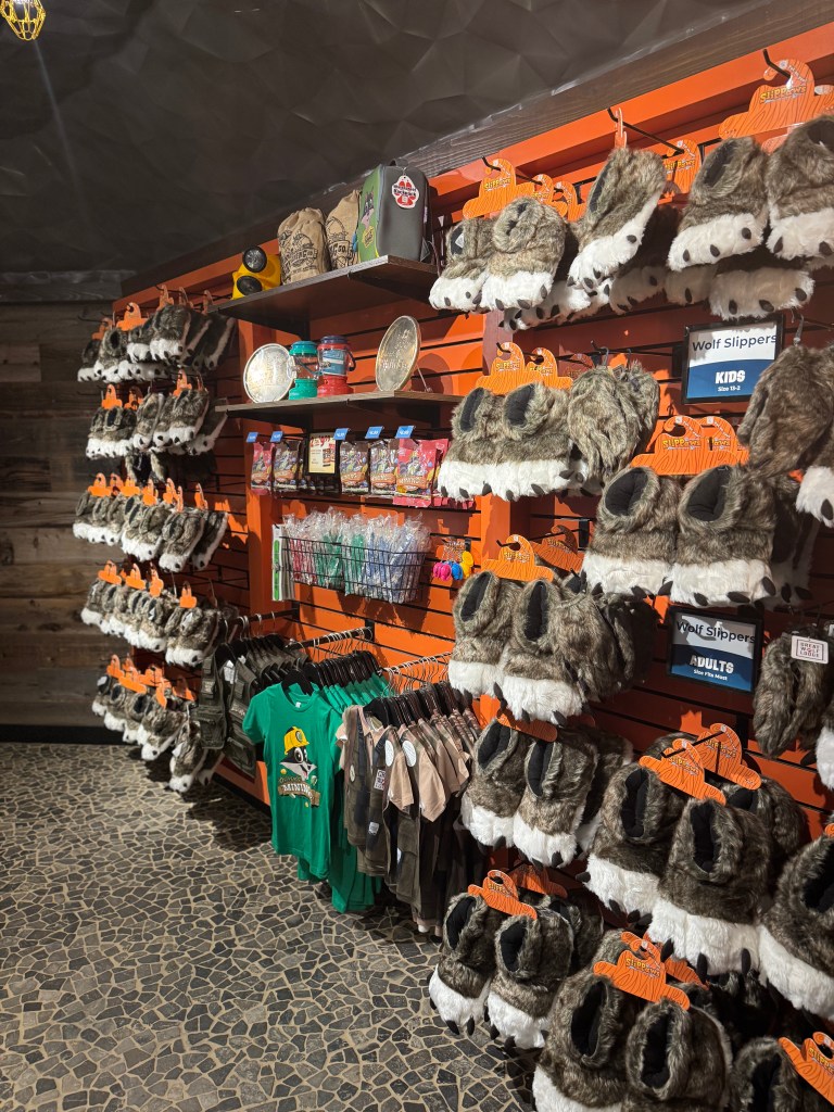 A shelf display at Great Wolf Lodge featuring various wolf slippers for kids and adults, with additional merchandise including T-shirts and toys.