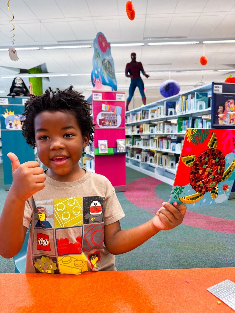 Smiling kindergartner giving a thumbs-up while showing his finished mosaic turtle.