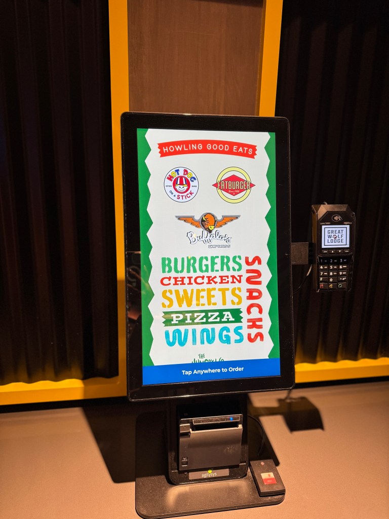 Digital menu display at Great Wolf Lodge showcasing food options including burgers, chicken, pizza, wings, and snacks.