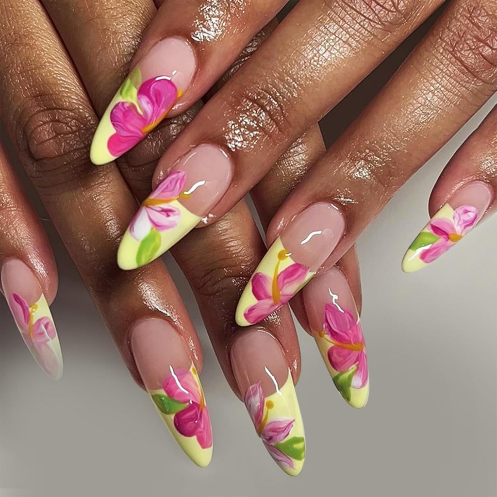 Close-up of elegantly manicured nails featuring yellow tips decorated with vibrant pink and green floral designs.