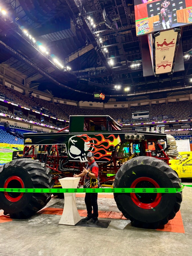 Bone Shaker driver stands beside the monster truck while signing autographs for families.