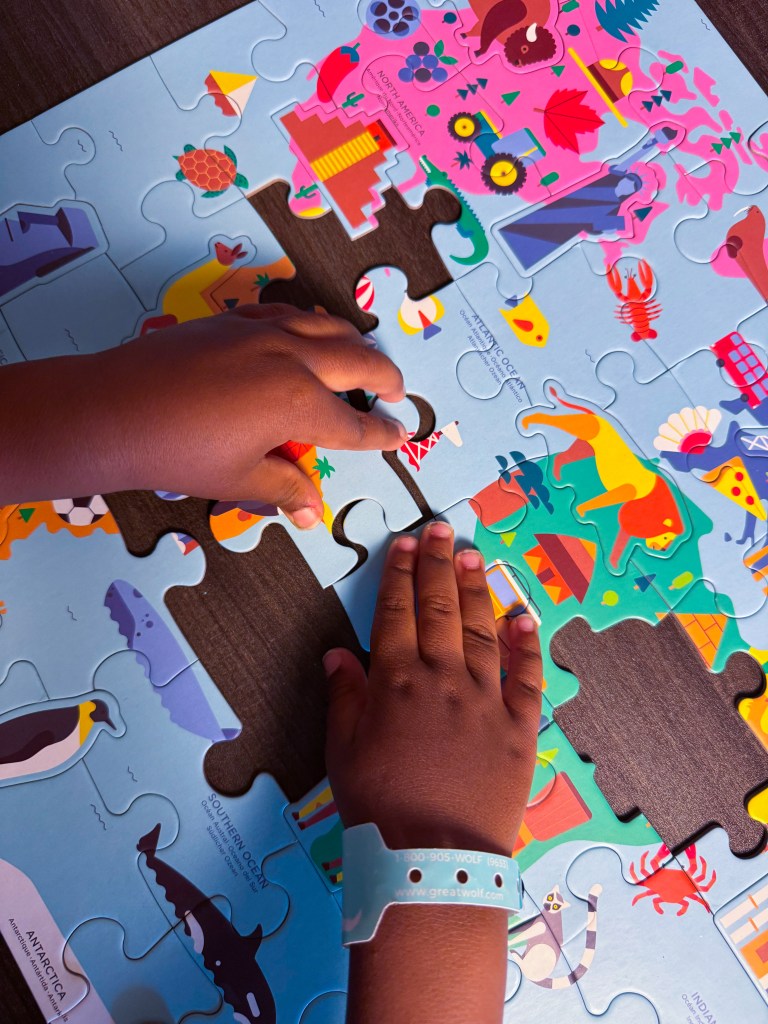 Child placing a colorful puzzle piece into a world map while learning about continents and landmarks.