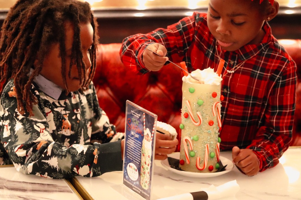 Children admiring Sugar Factory Biloxi's holiday milkshake decorated with whipped cream, candy canes, and a gingerbread house.